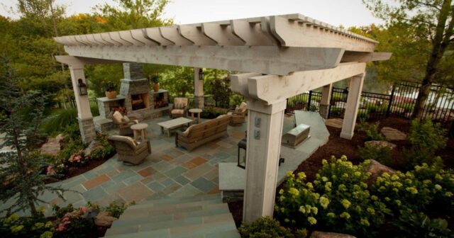 White wooden pergola over an outdoor living area with fireplace, seating area and kitchen