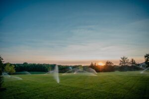 large green space with multiple sprinklers watering the lawn during sunset