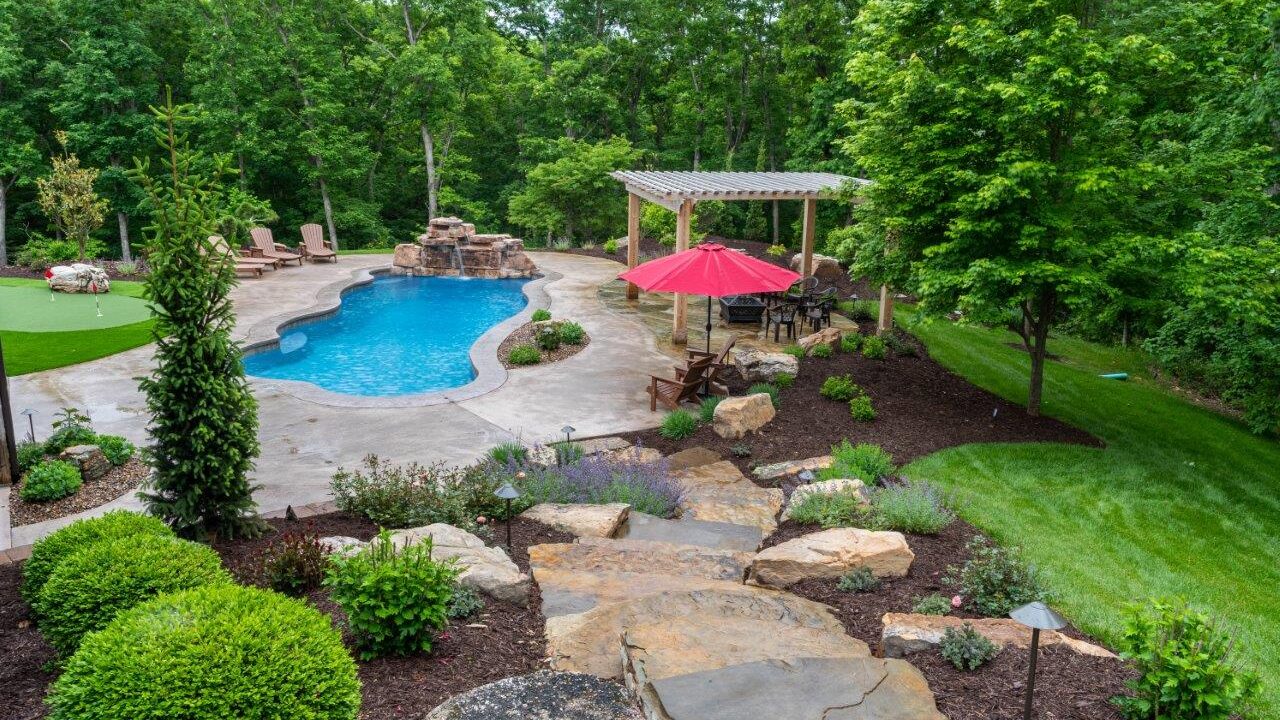 view of pool with stone waterfall and pergola from to of stairs.
