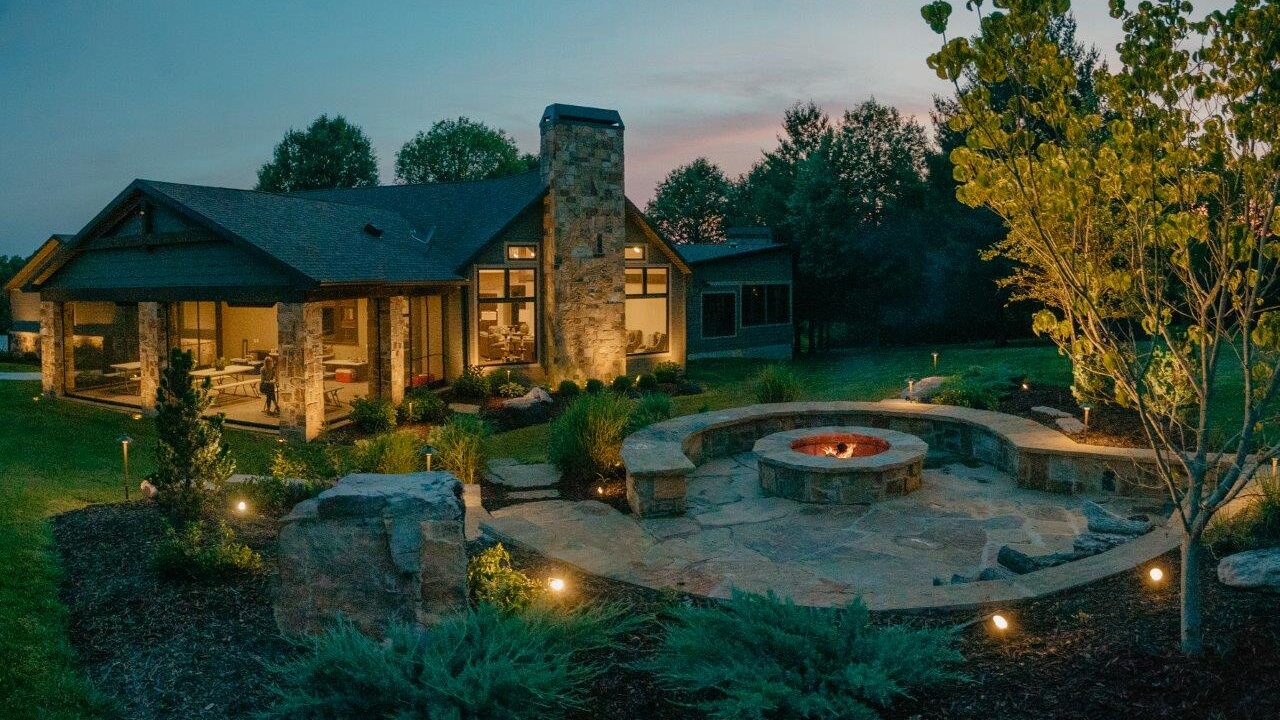 outdoor firepit with stone patio and seating with house in background at sunset