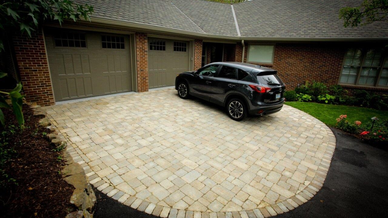 car parked in front of garage attached to house on driveway made of pavers