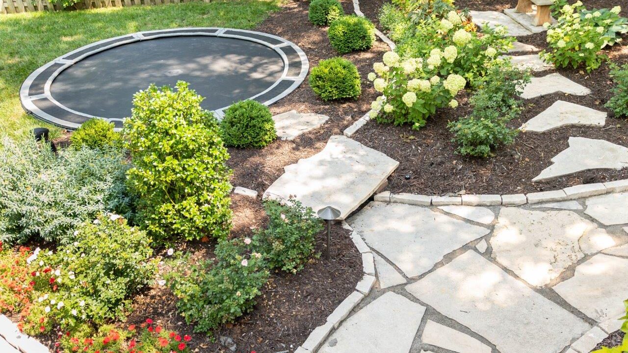 stone walkway with landscaped beds and in ground trampoline