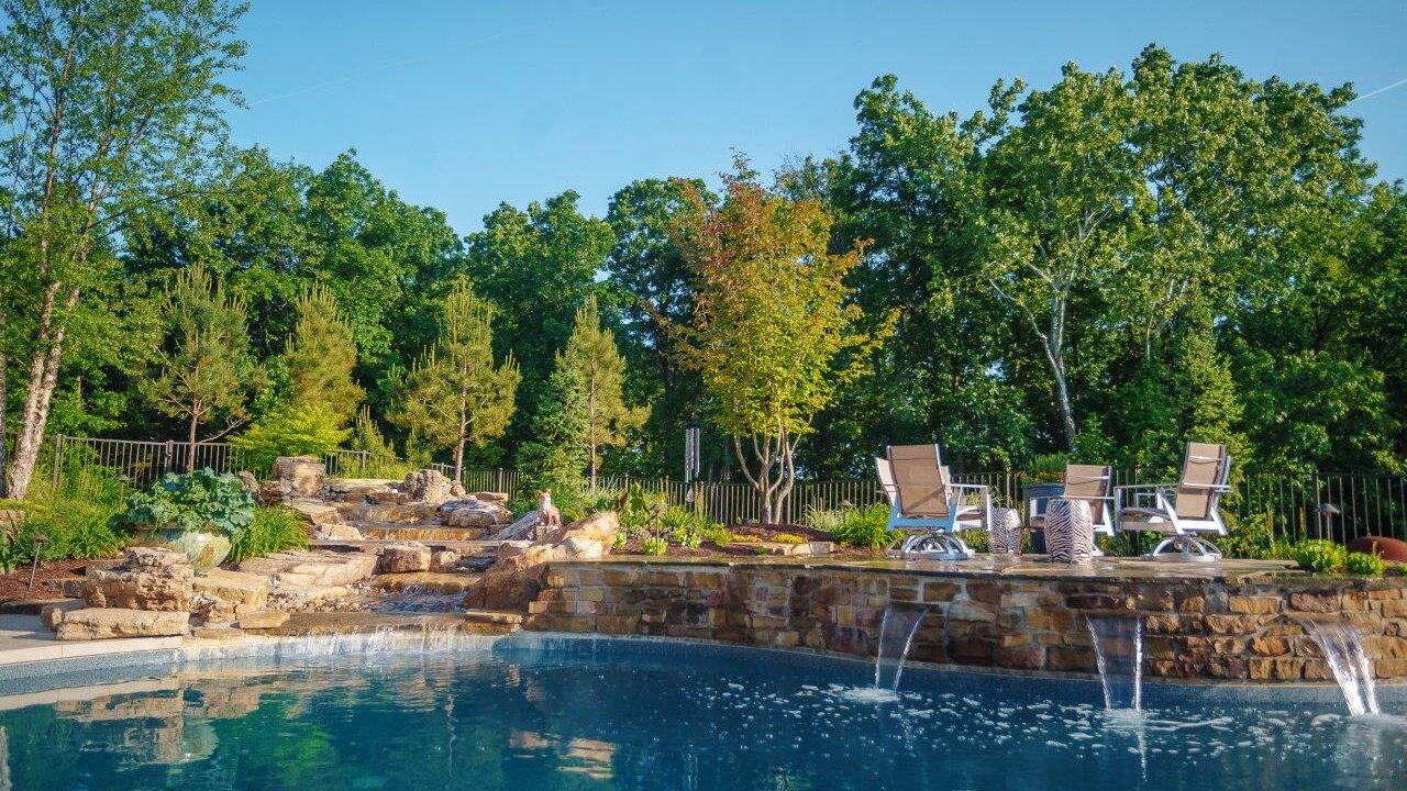 pool with stone waterfall and seating with trees in the background
