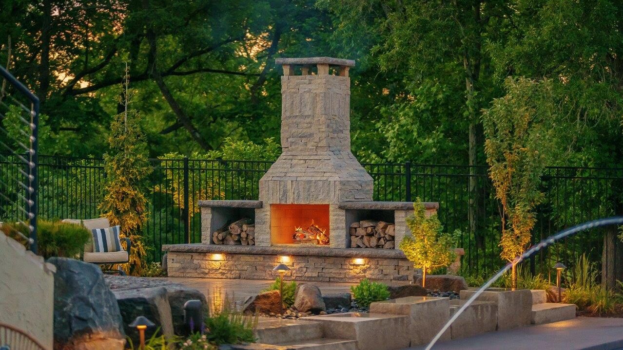 outdoor stone fireplace with chimney and log storage