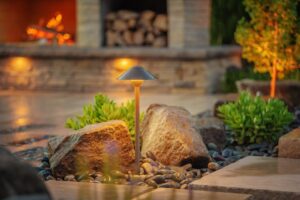 outdoor lights in a landscaped bed with rocks and greenery with blurred outdoor fire place in background