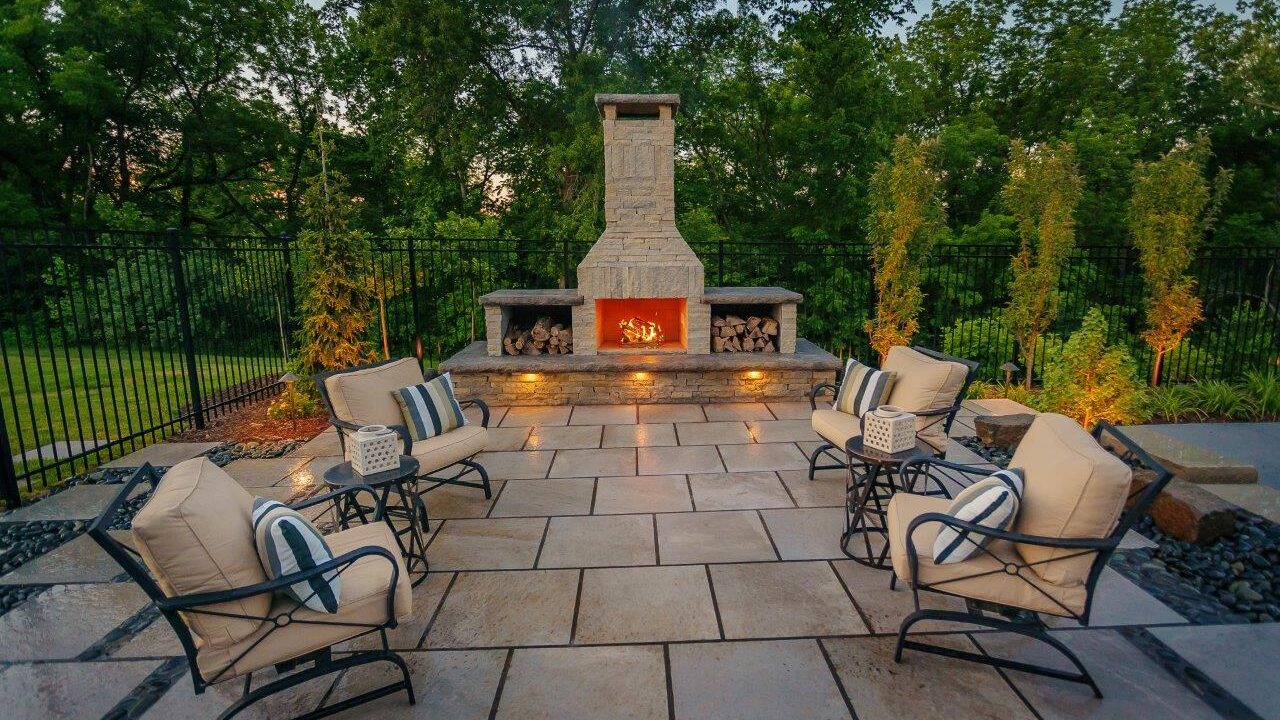 outdoor stone fireplace on patio with seating and trees in the background