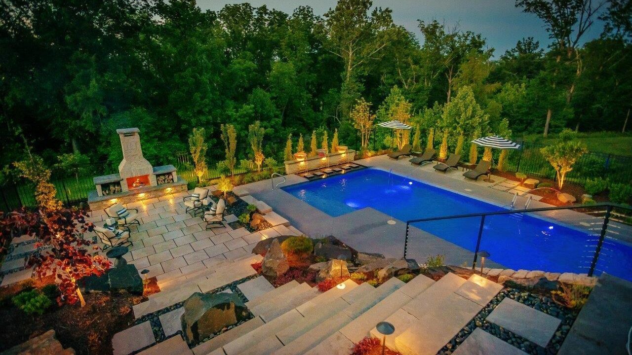 view of outdoor pool and fireplace from top of stairs