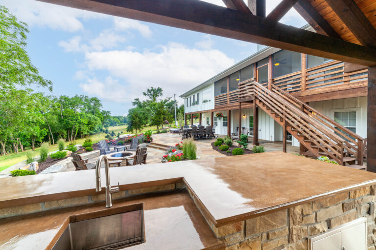 sink and stone counter in outdoor kitchen overlooking flagstone patio, multiple seating areas, and house