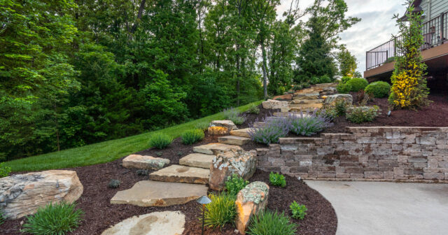 rock steps in a hill side behind a house surrounded by green shrubs