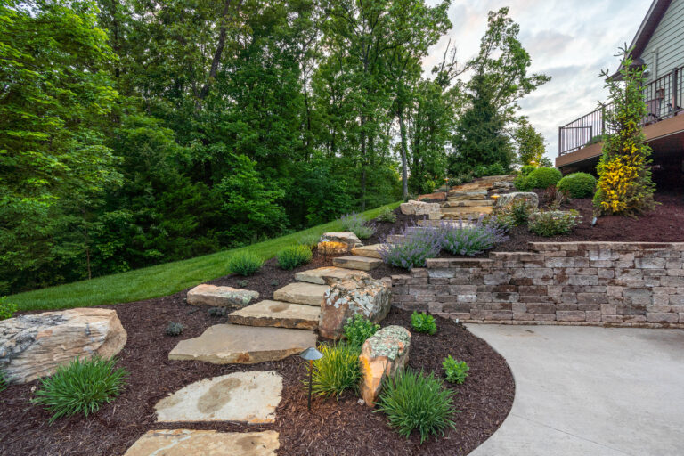 rock steps in a hill side behind a house surrounded by green shrubs