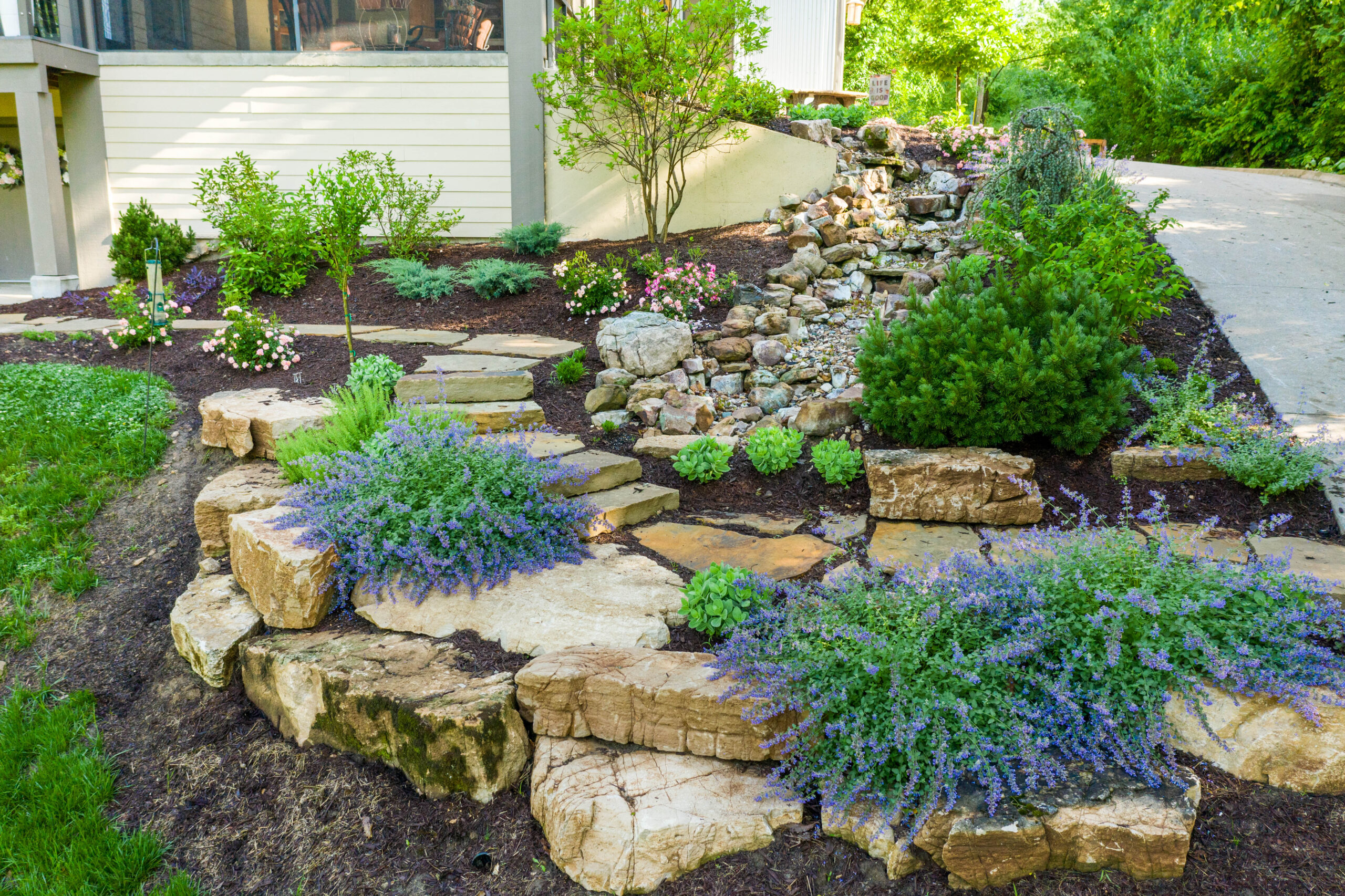 Stone paver walkway from driveway to door with landscaping on either side.